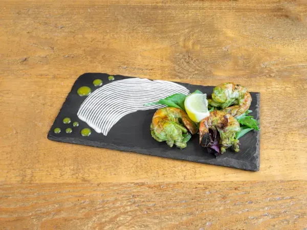 Plated crab cakes with cucumber slice and greens on a black slate board with sauce dots.