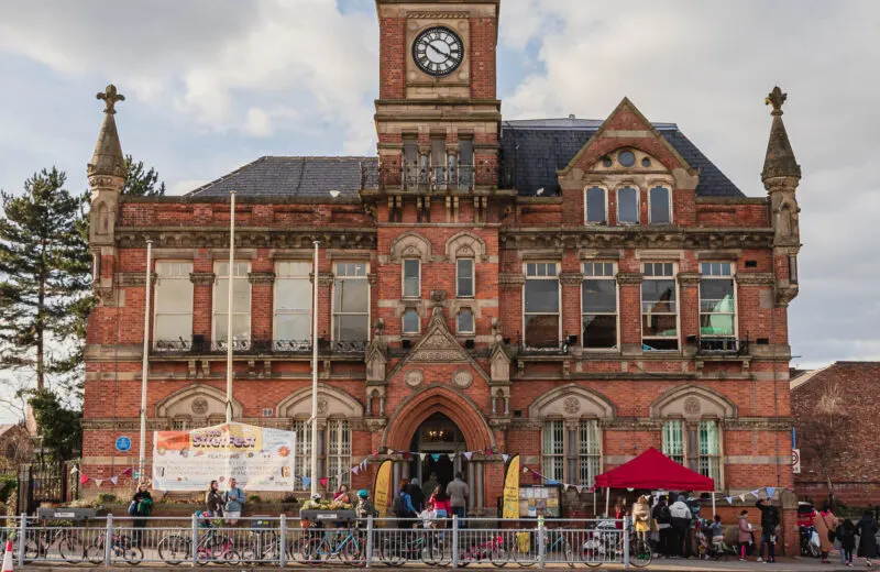 A Victorian red brick building with a clock tower, with visitors and a red marquee at its entrance during daytime.