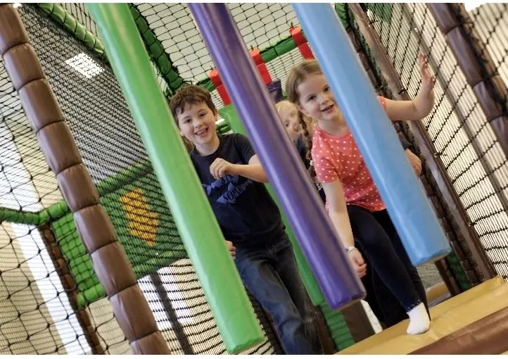 Two young children playing inside a colourful soft play structure with foam pillars.