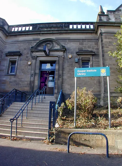 Stone library building with blue entrance sign, metal railings and steps leading to the front door.