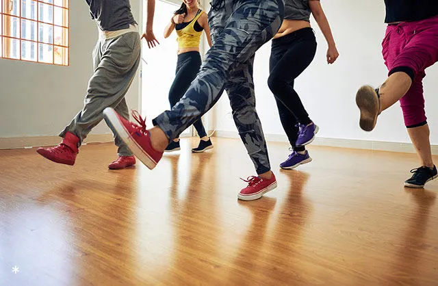 A group of people exercising together on a wooden floor in a bright studio space.
