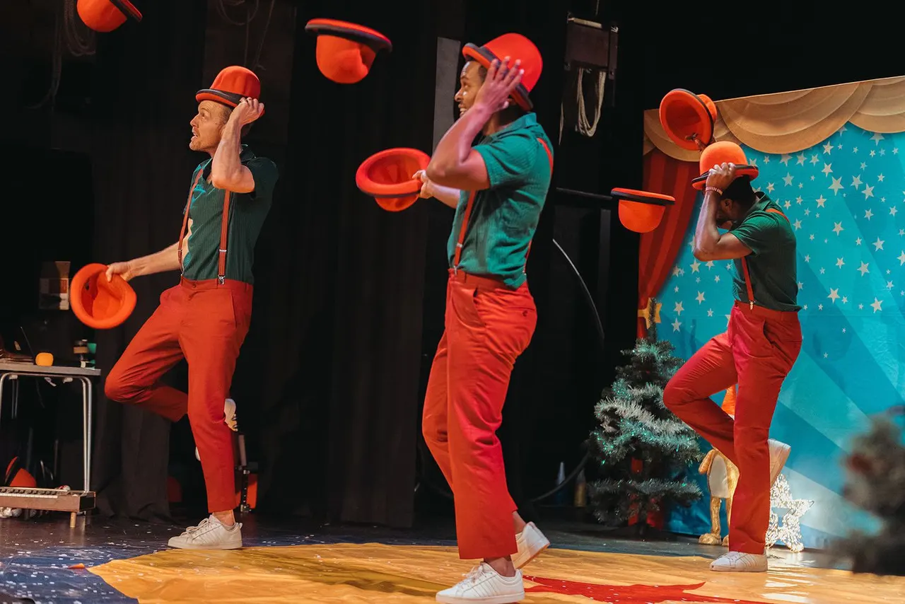 Circus performers in red costumes and hats juggle buckets on stage during a live performance.
