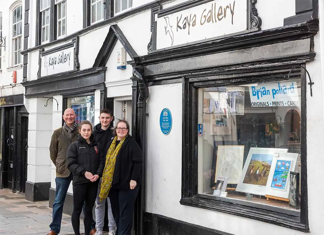 Four people standing outside Kaya Gallery, a street-level art gallery with black timber framing and white walls displaying artwork in the window.