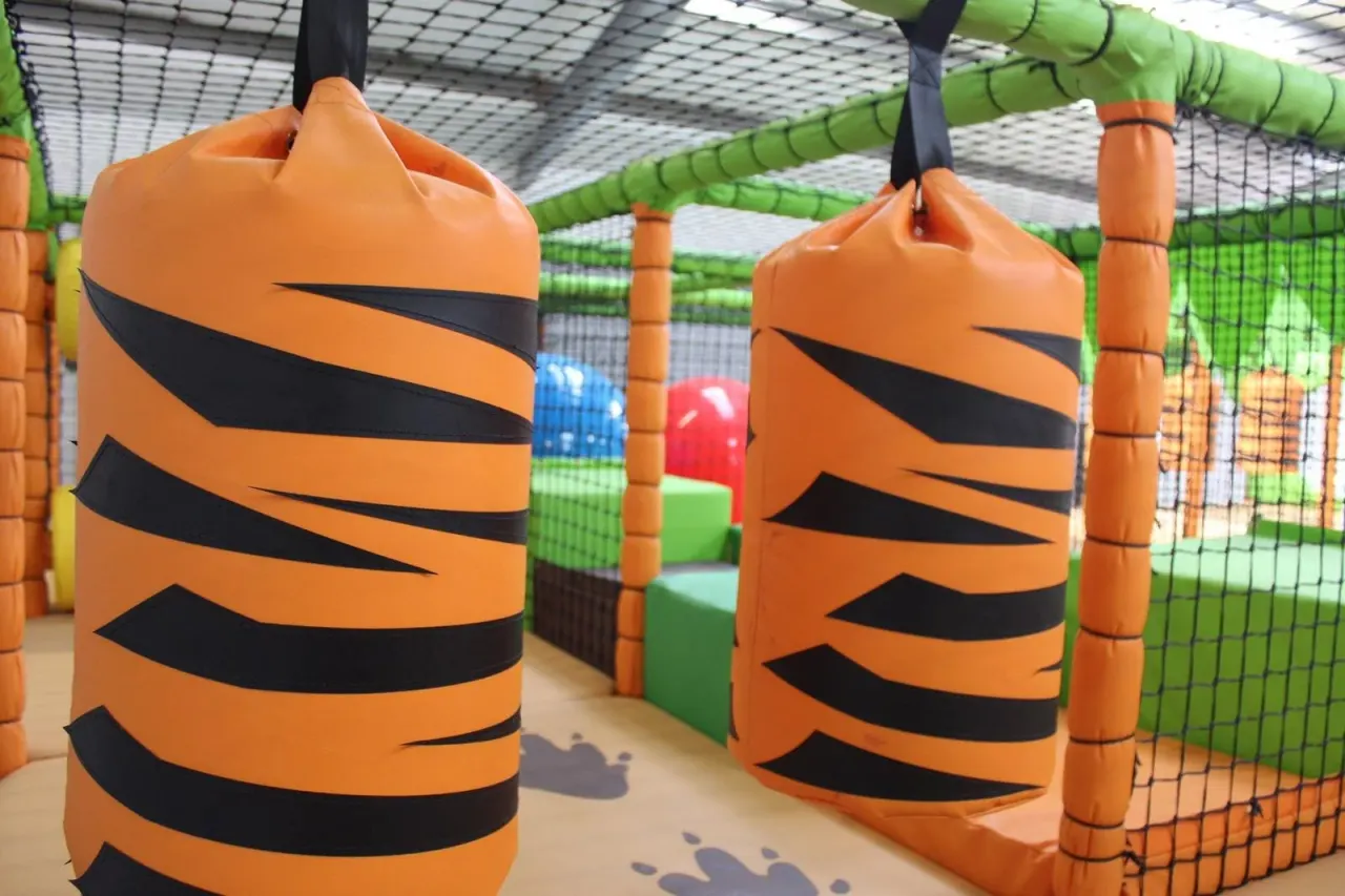 Inflatable obstacle course with orange and black striped tunnel sections and green netting inside an indoor play area.