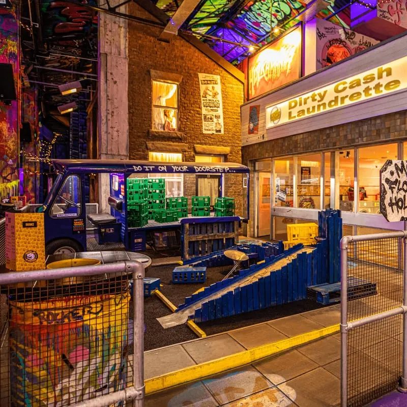 Indoor mini golf course with colourful obstacles, arcade machines and neon lighting in an urban setting.