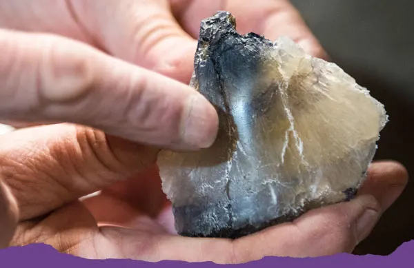 Person's hands holding a dark grey and pale crystalline mineral specimen.