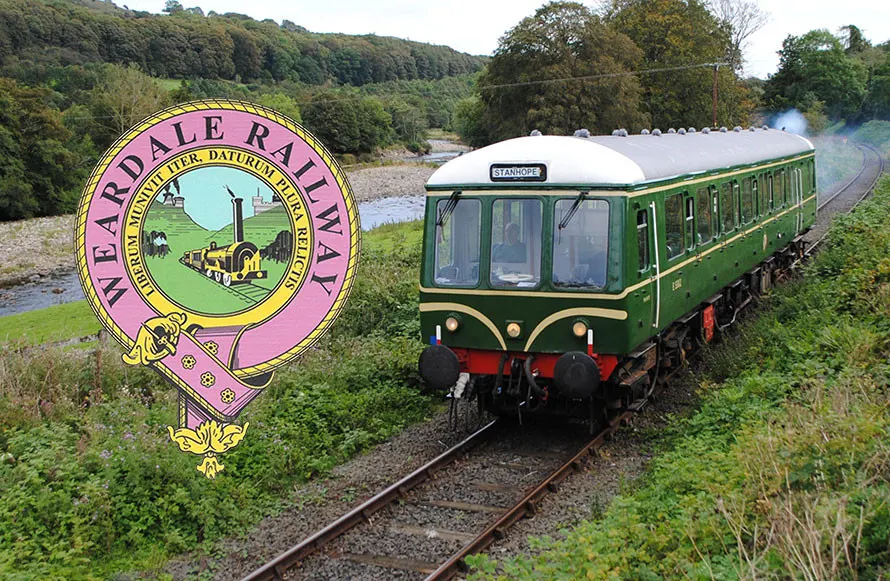 A green and cream heritage railway carriage on tracks beside a river valley with wooded hillsides.