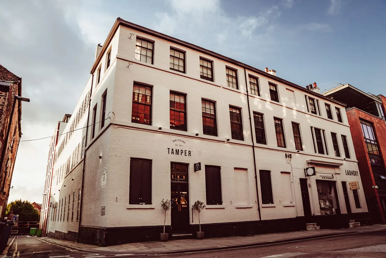 Historic white-painted corner building with red-brown trim and windows, housing Tamper venue on ground floor.