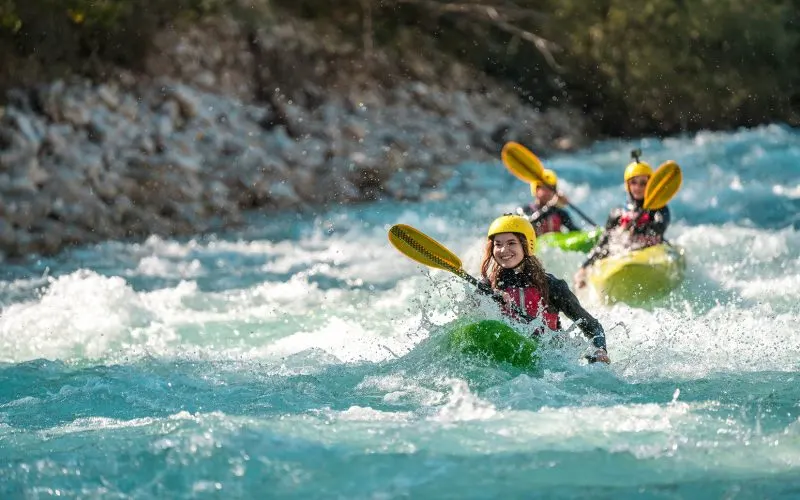 Group of people whitewater kayaking on a turquoise river with rapids and rocky cliffs.