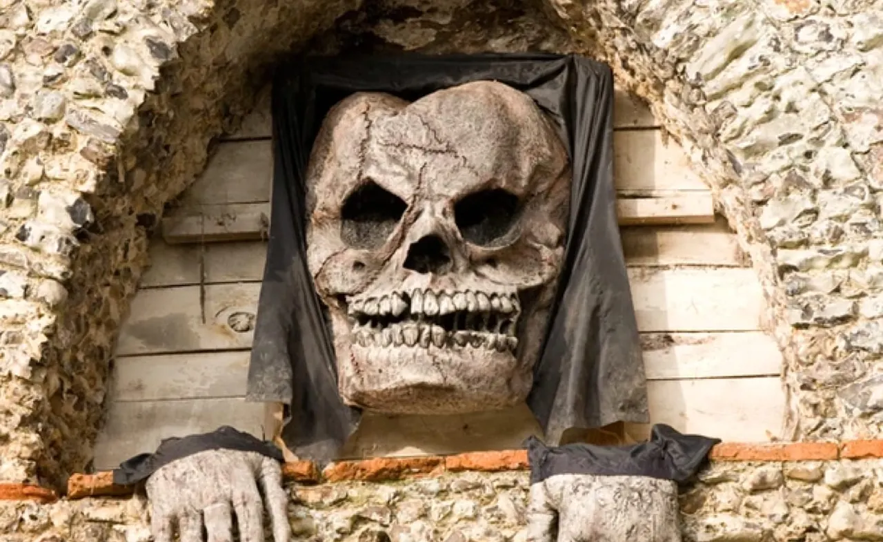 A large skull sculpture with draped black fabric mounted on a stone wall within a cave.