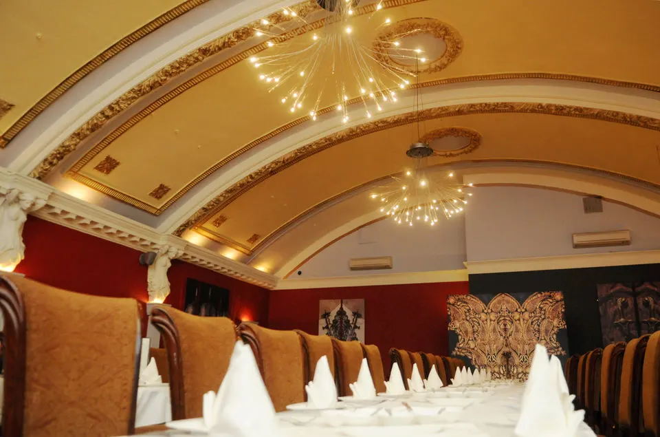 Elegant dining room with ornate ceiling, decorative pendant lights, and formally set tables with white napkins.