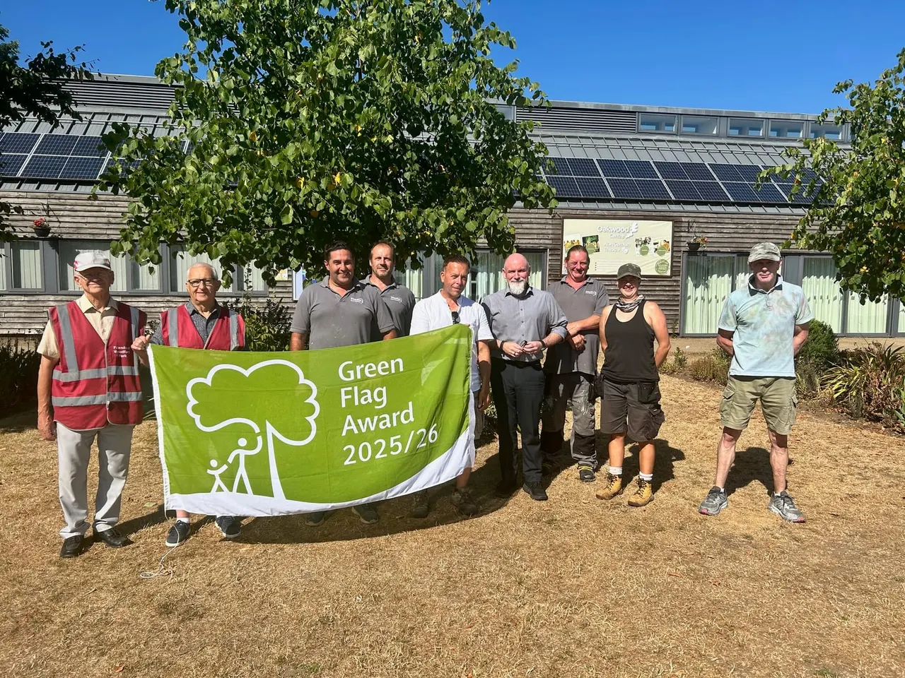 Group of staff and volunteers holding a Green Flag Award banner outside a sustainable building with solar panels.