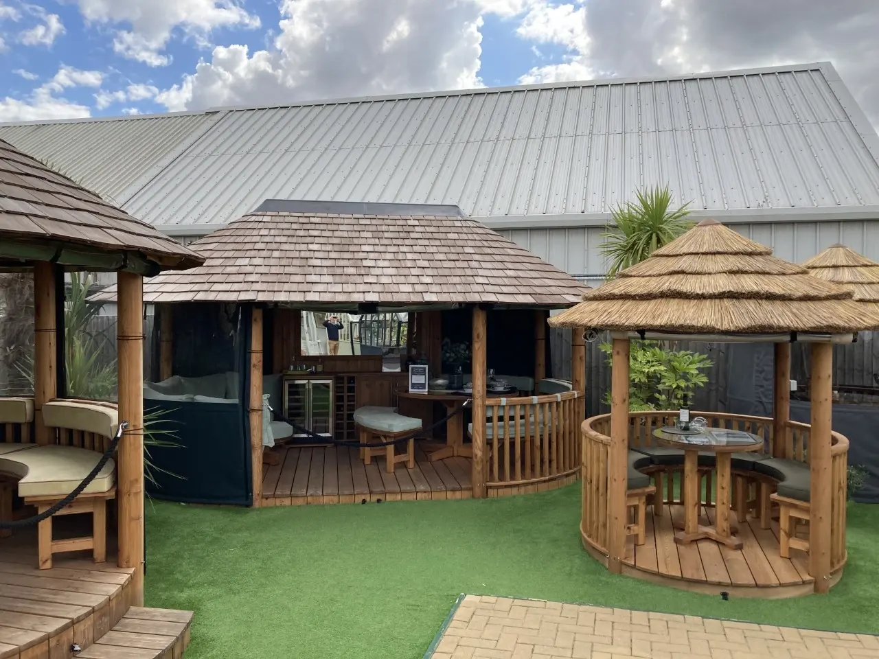 Outdoor spa and leisure pavilions with wooden gazebos, thatched roofs, and decking overlooking manicured lawn.