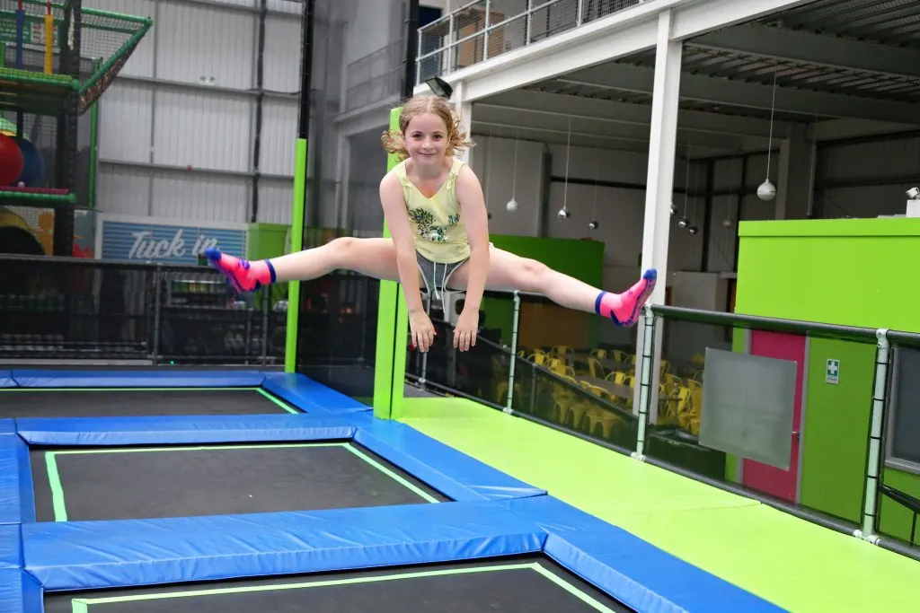 Young girl performing a split in mid-air on a trampoline at an indoor play centre.