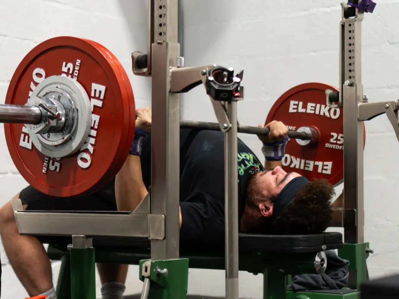 Man performing bench press with red Eleiko weight plates at a gym.