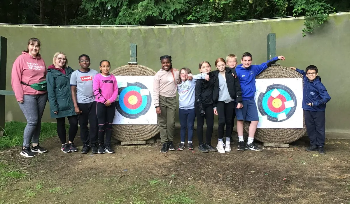 Group of young people posing together at an outdoor archery range with straw targets.