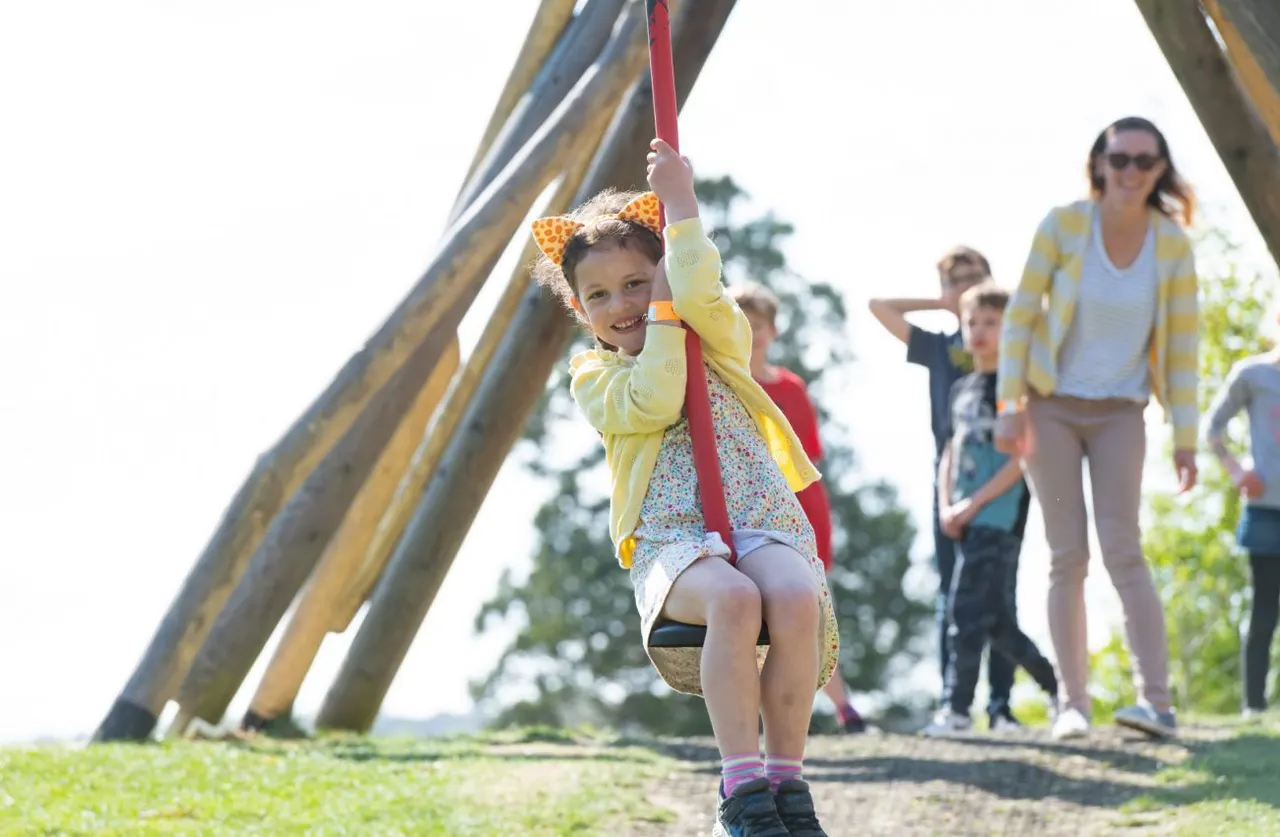 Child swinging on a rope swing whilst adults supervise outdoors at a leisure venue.