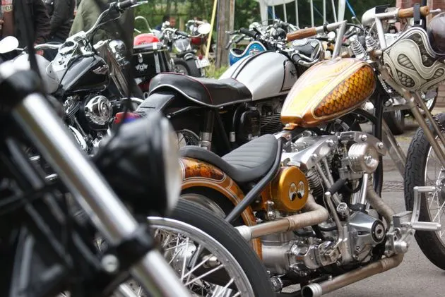Row of customised motorcycles parked outdoors at a gathering, featuring chrome details and decorative paint work.