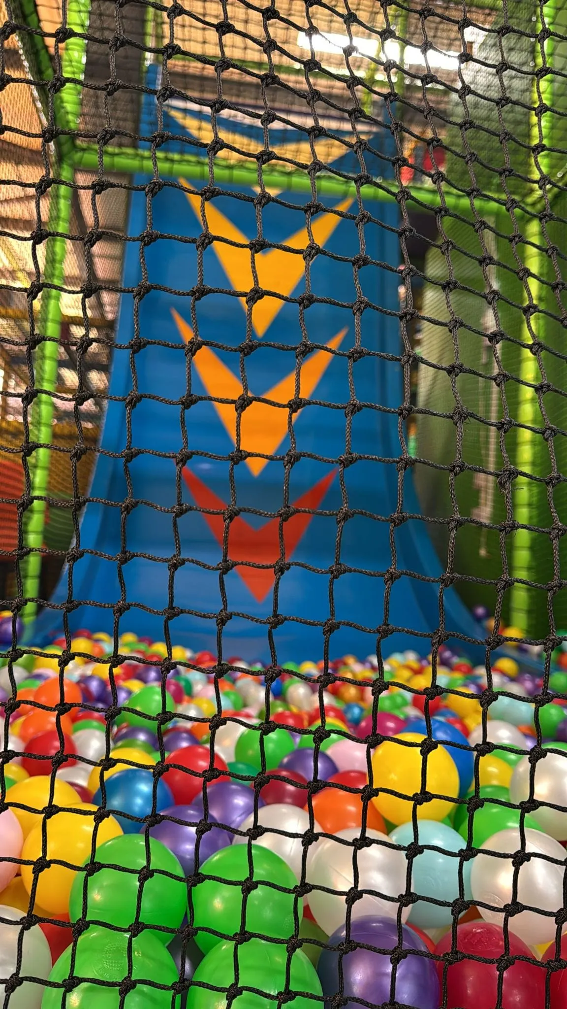 Black netting encloses a colourful ball pit with bright balls in red, yellow, green, blue and purple.
