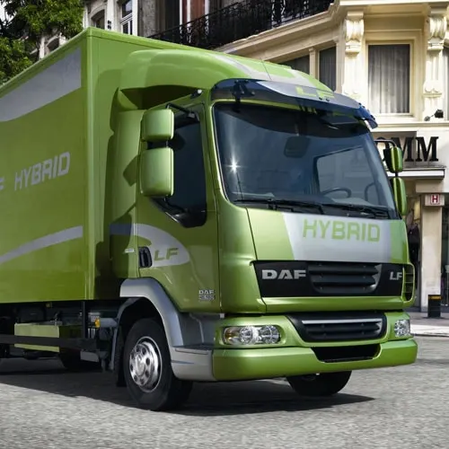 Green and grey DAF hybrid delivery truck parked on a stone street in front of period buildings.
