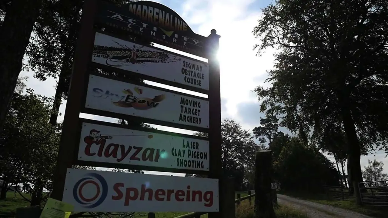 A directional sign mounted on a pole listing activity attractions, surrounded by trees on a leisure venue grounds.