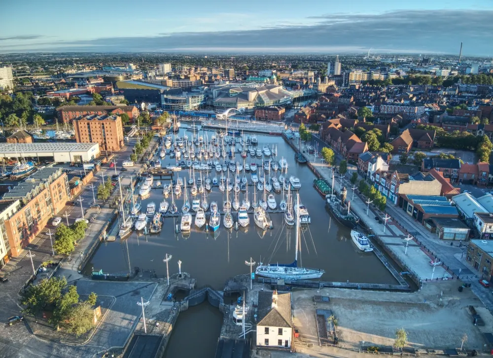 Aerial view of a busy marina with dozens of moored sailing boats and larger vessels in a city waterfront setting.