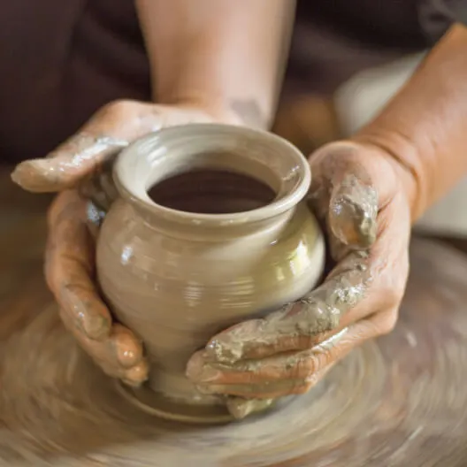 Hands holding a freshly made clay pot on a pottery wheel.