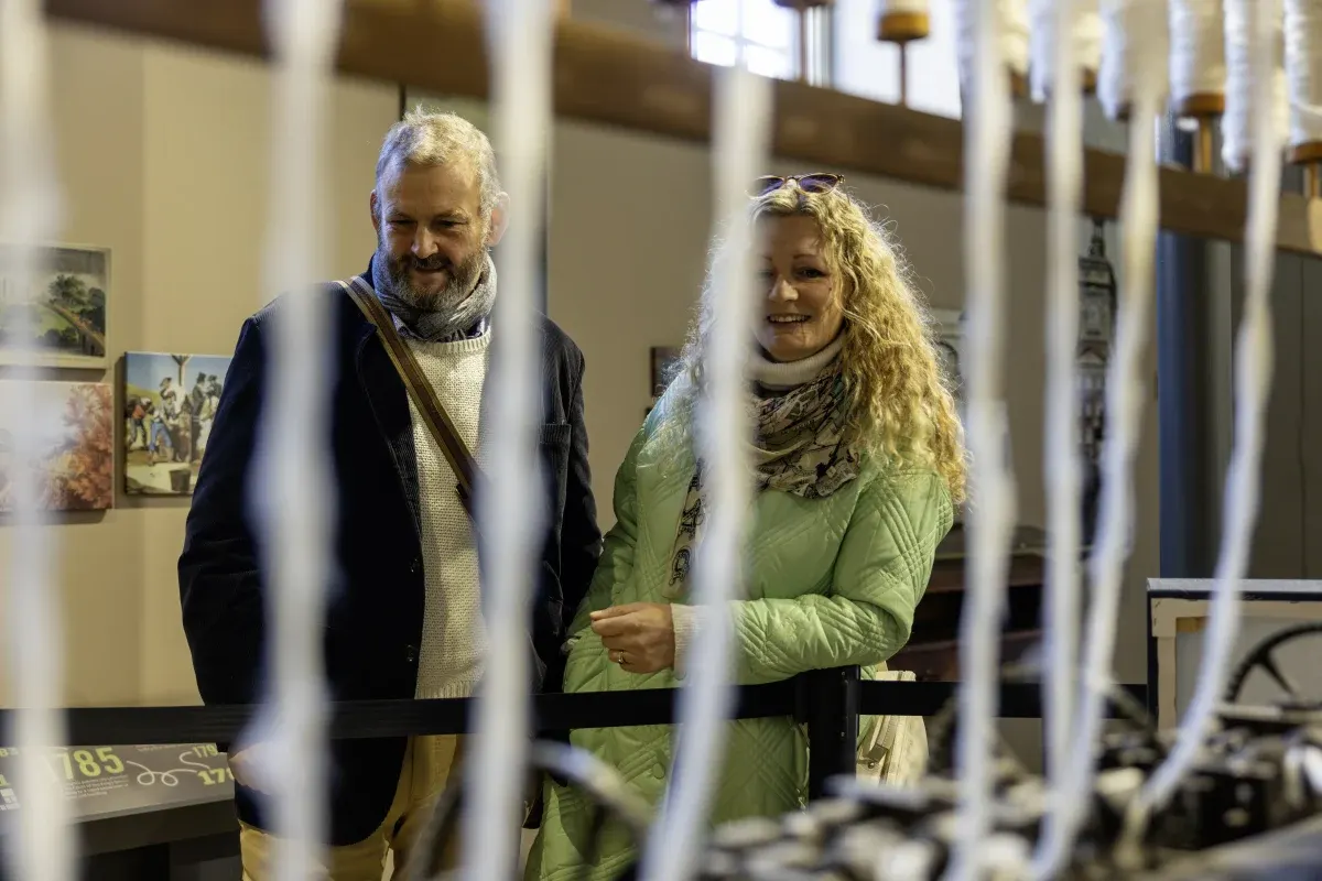 Two visitors viewing exhibits behind glass in a museum gallery with cream-coloured walls and display cases.
