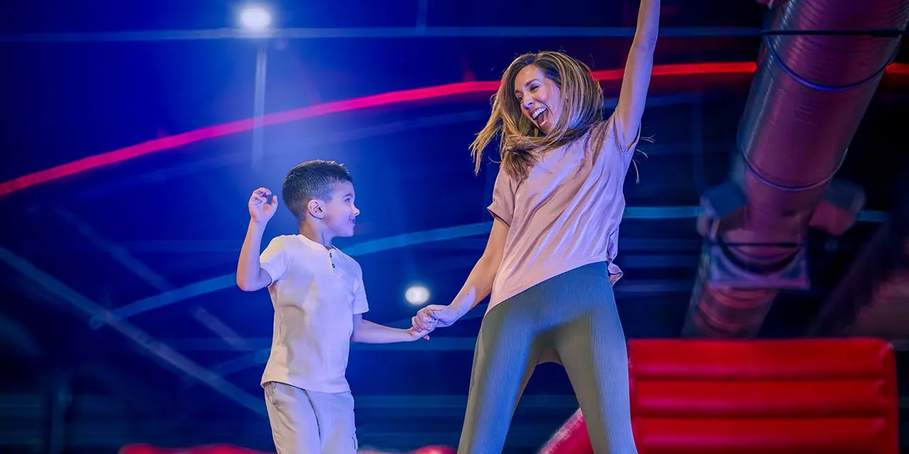Woman and young boy dancing together on a lit dance floor with red and blue neon lighting.