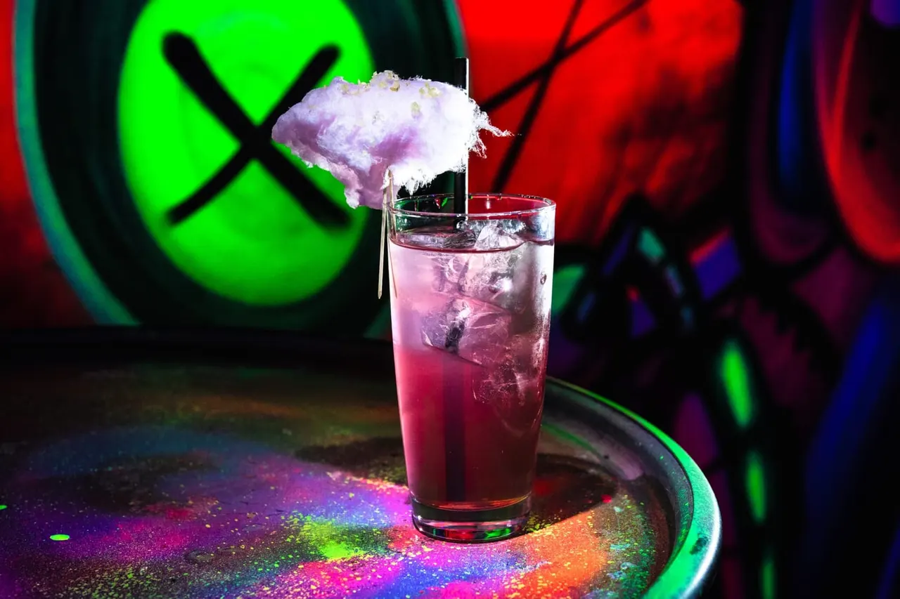 Colourful cocktail with cotton candy garnish under vibrant neon lights in a nightlife venue.