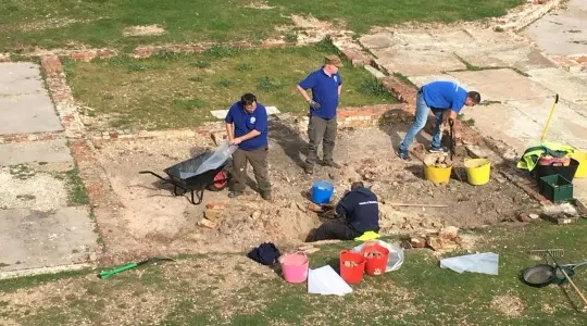 Group of people in blue shirts doing groundwork and excavation at an outdoor archaeological or construction site.