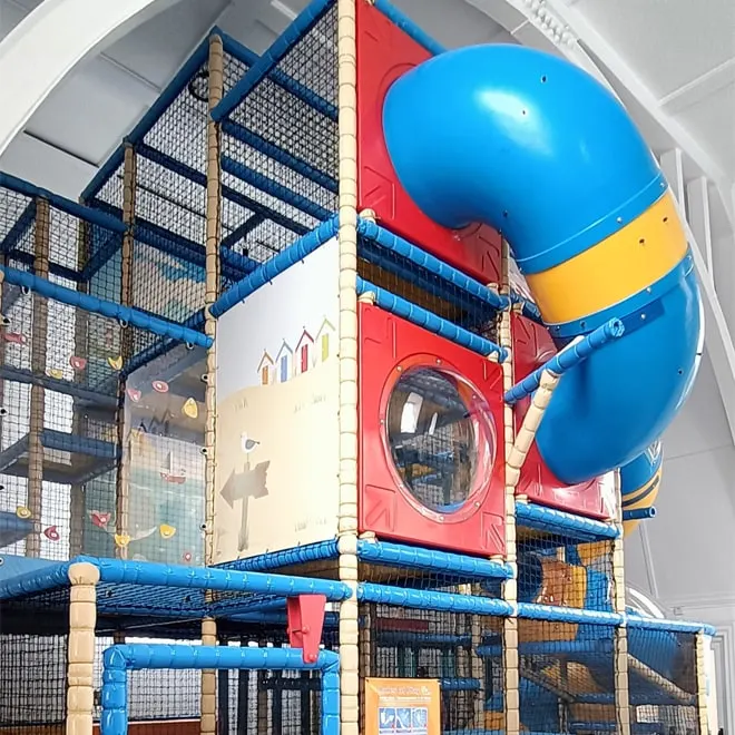 Large indoor soft play structure with blue ball pit, red slide tower and climbing frame in leisure centre.
