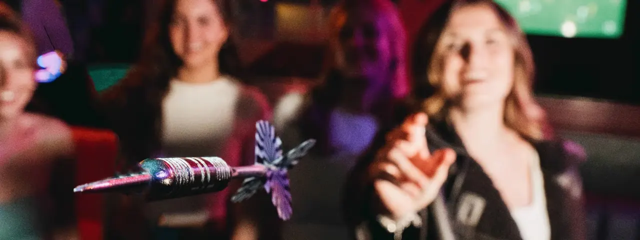 People singing and socialising in a dimly lit bar with colourful lighting and a decorative microphone in sharp focus.