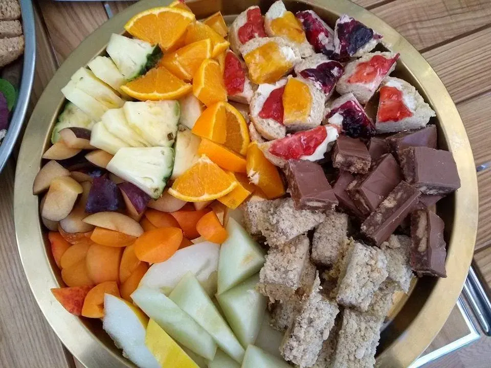 Overhead shot of a round platter with fresh fruit, chocolate pieces, small cakes, and biscuits arranged in sections.