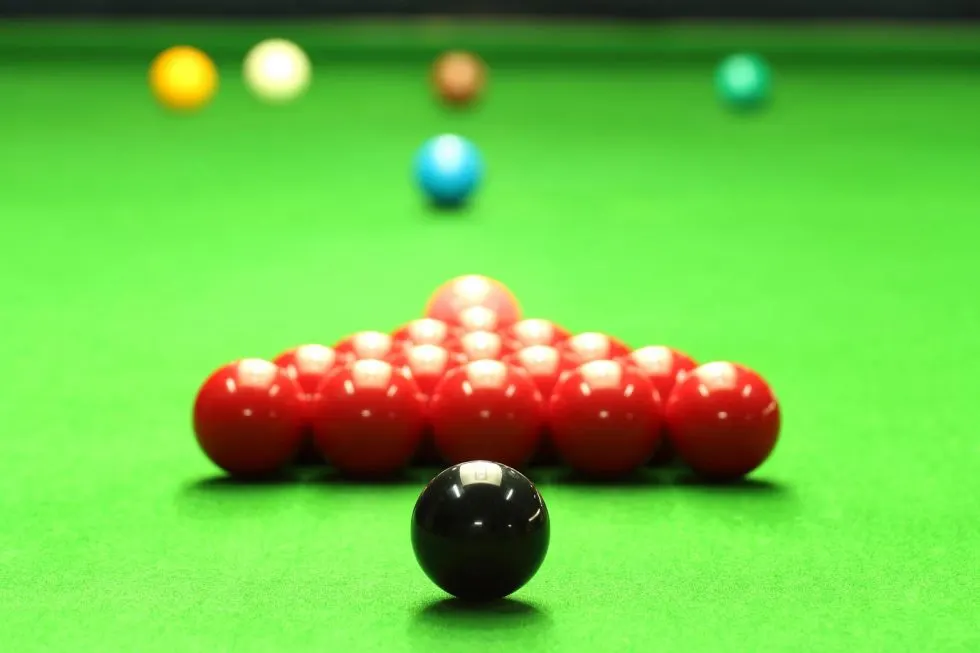 Snooker balls arranged on a green baize table, with the black ball in front of a pyramid of red balls.