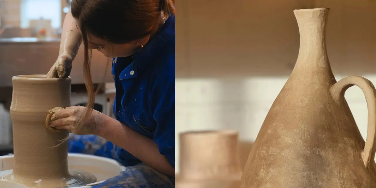 Potter shaping clay on a wheel while wearing a blue apron in a sunlit studio.