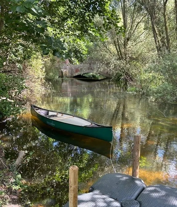 Moored boats on a calm tree-lined river with dappled sunlight reflecting on the water.