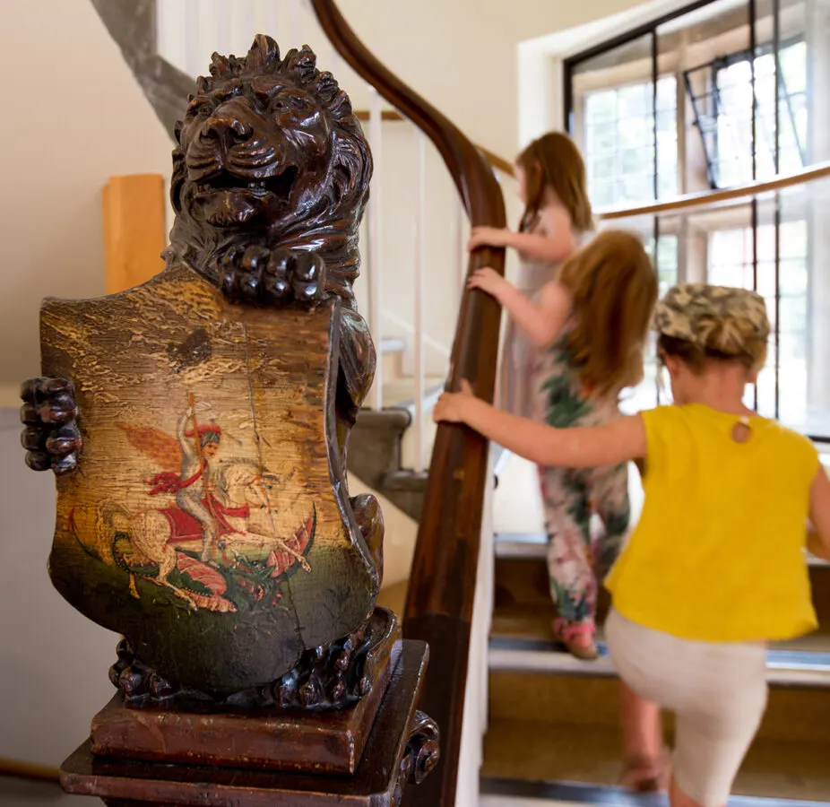 Carved wooden lion statue with decorative painted base displayed indoors, with visitors in background.