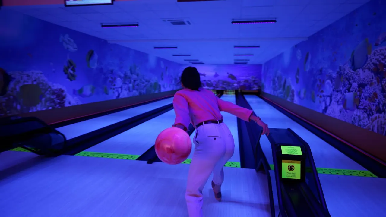 Person in pink clothing bowling on a glow-in-the-dark lane with vibrant blue and purple lighting and coral reef murals on walls.