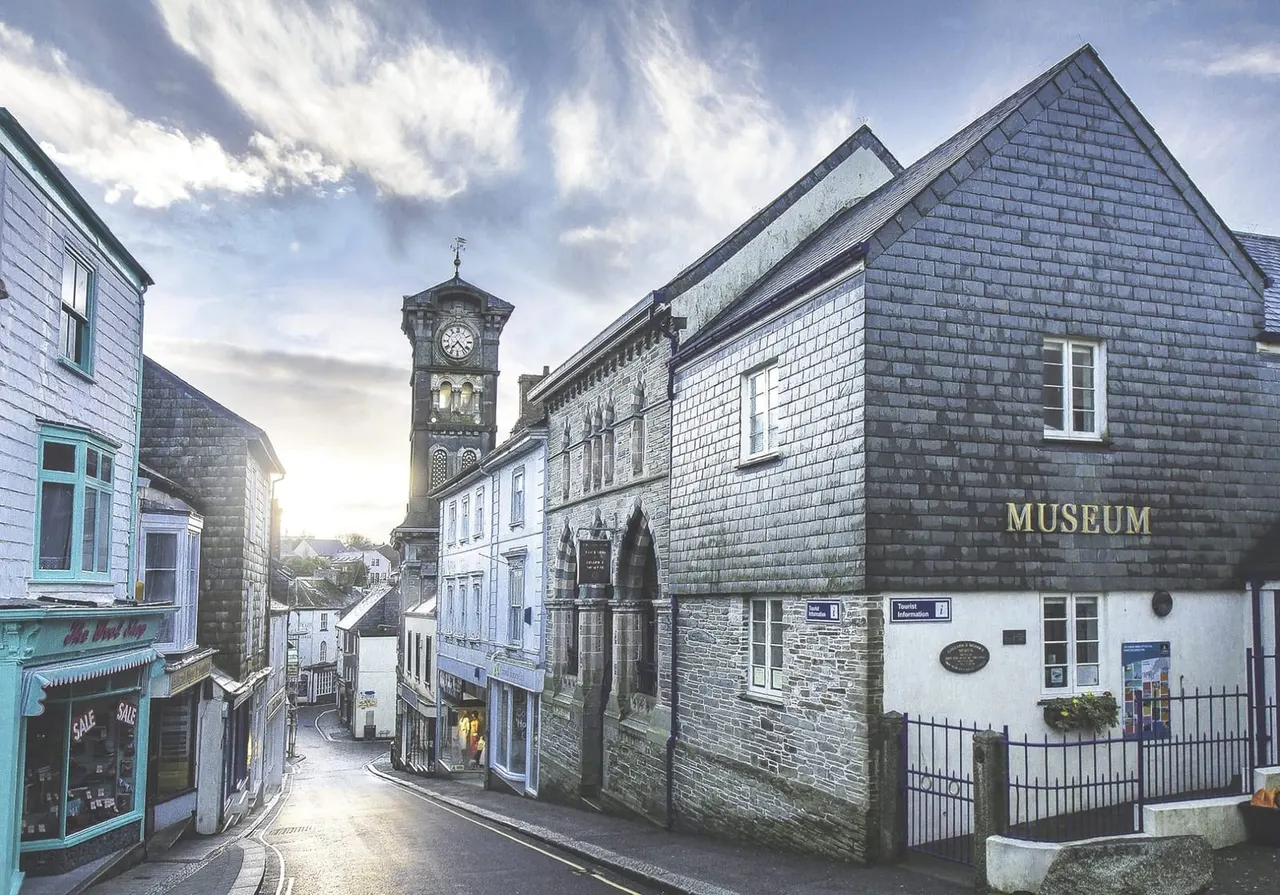 Historic stone buildings line a quiet street, with a clock tower visible in the distance and a museum building marked on the right.