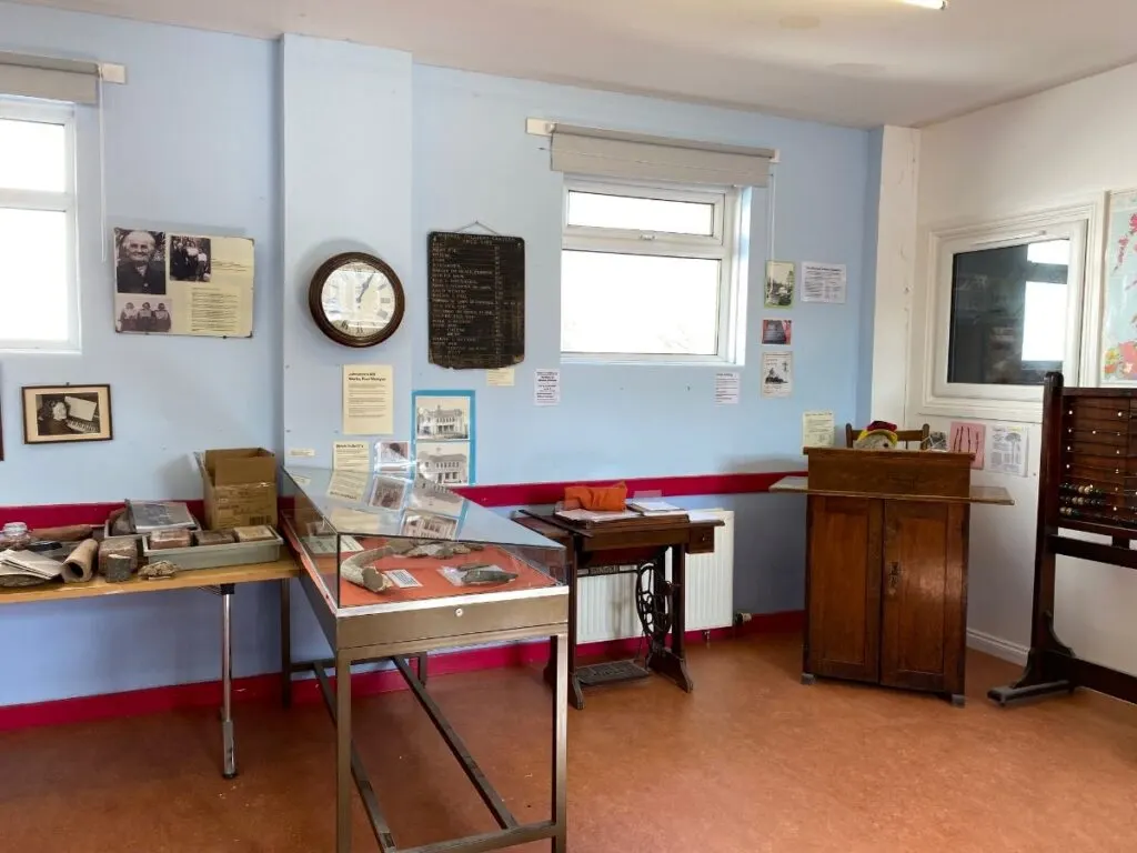 Museum display room with exhibition cases, antique furniture, historic photographs and memorabilia mounted on blue walls.