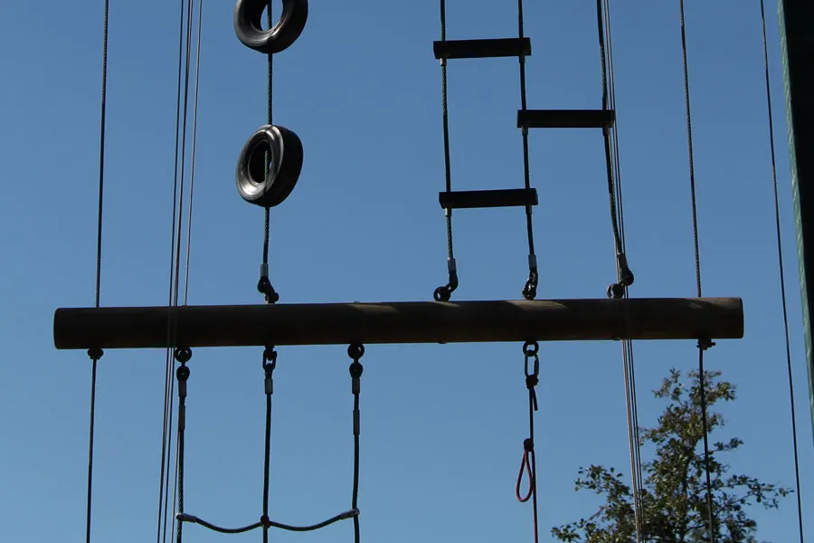 Outdoor adventure obstacle course equipment with tyre swings, rope ladder and ropes against blue sky.