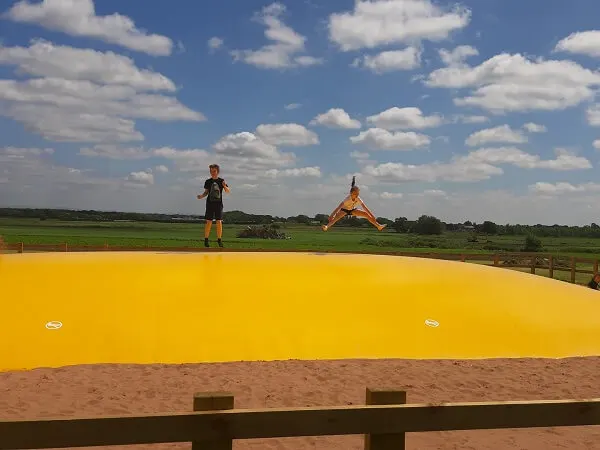 Person standing in a field with a large yellow inflatable and yellow kite against a blue sky.