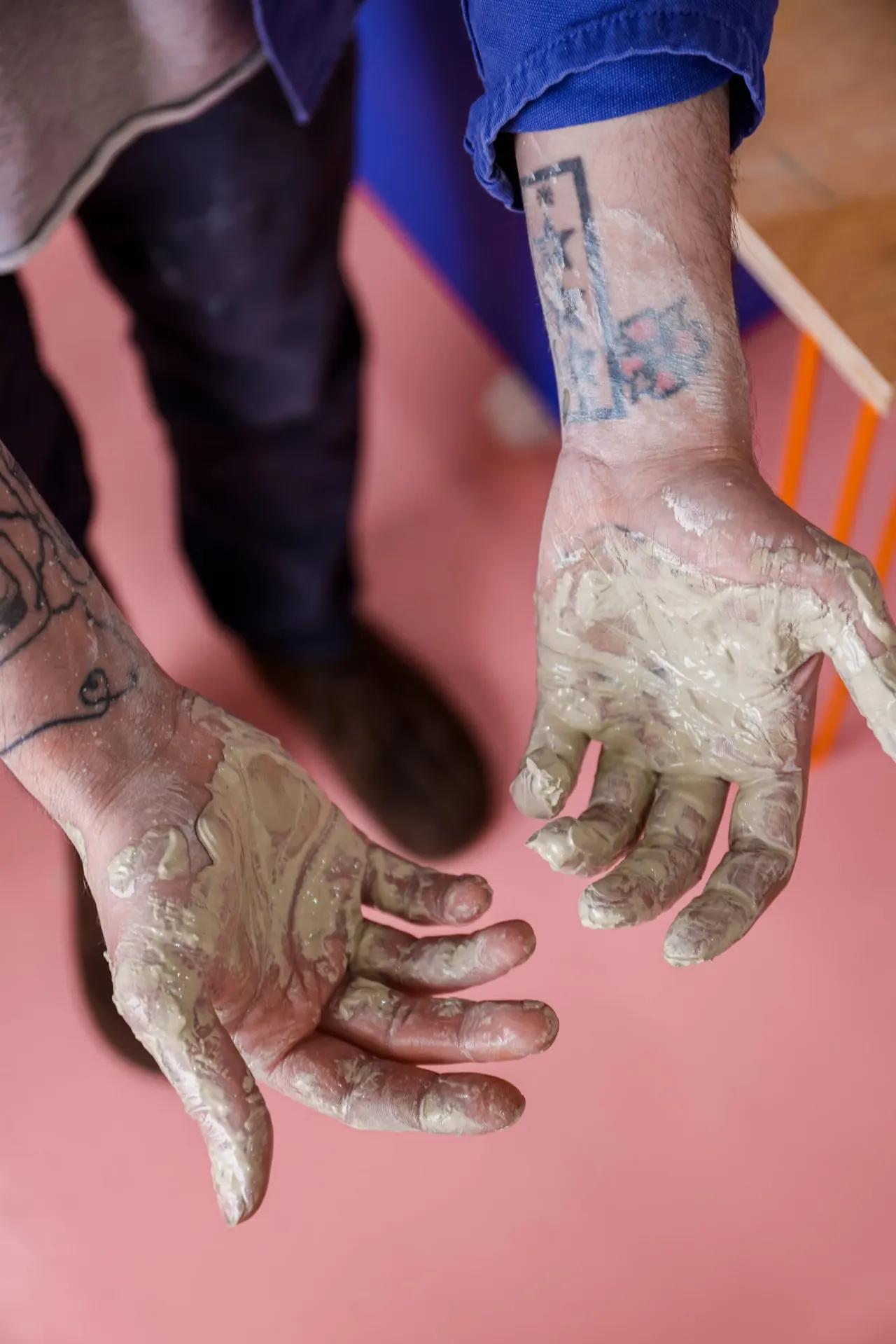 Person with clay-covered hands during a pottery or ceramics session at a studio.