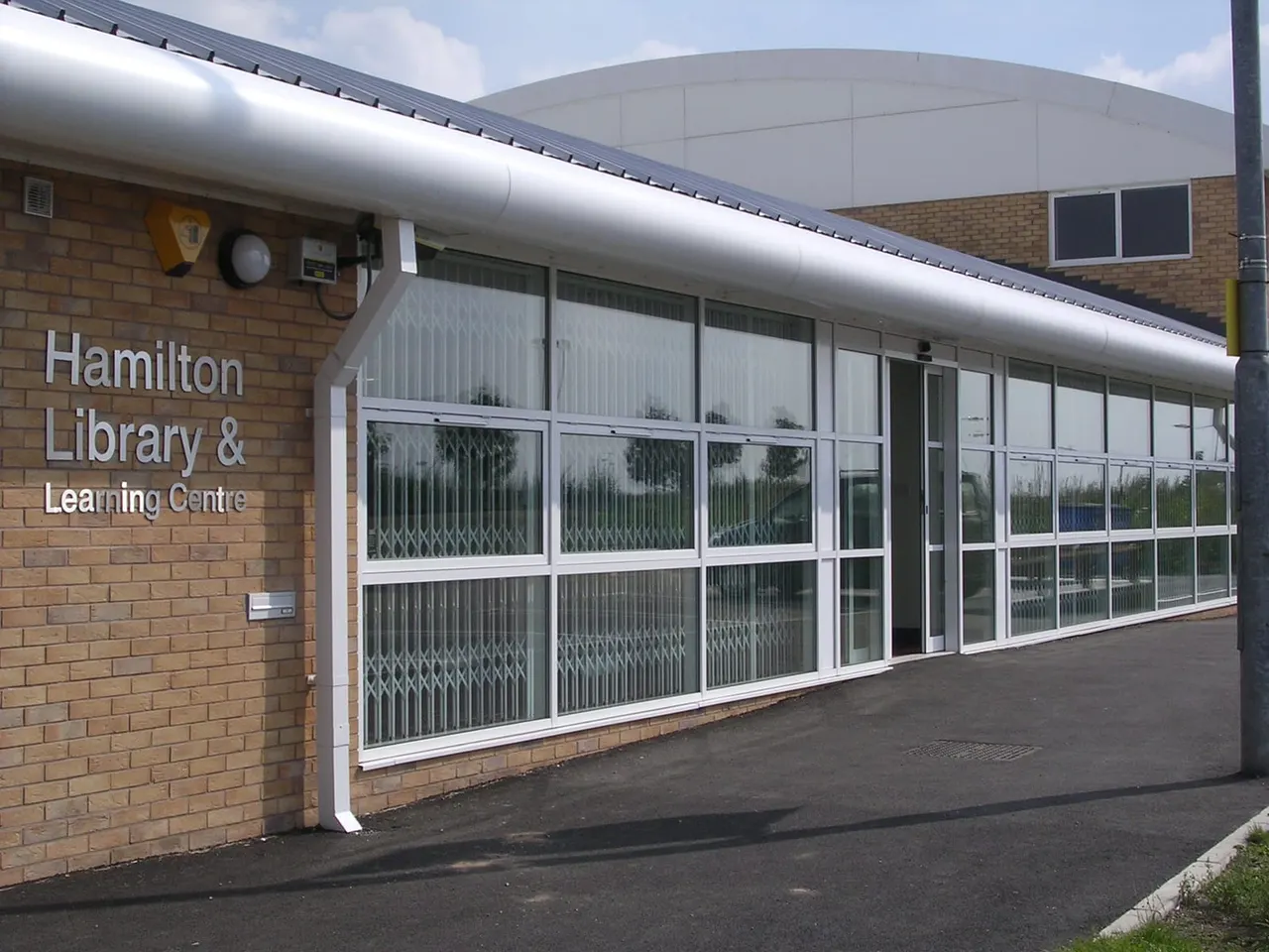 Exterior of a modern brick library building with large glass windows and white metal framing under a curved roof.