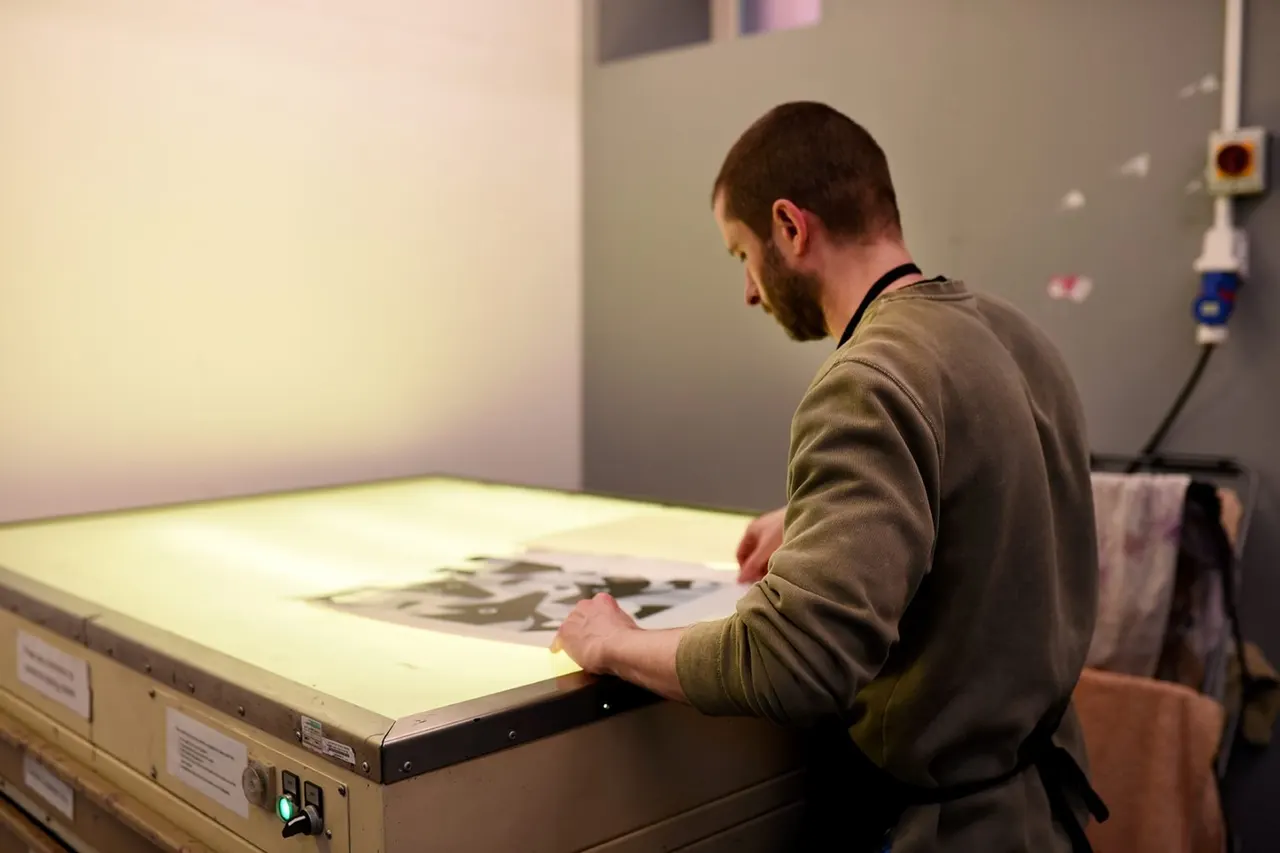 Man examining artwork on an illuminated lightbox table in a print workshop studio.