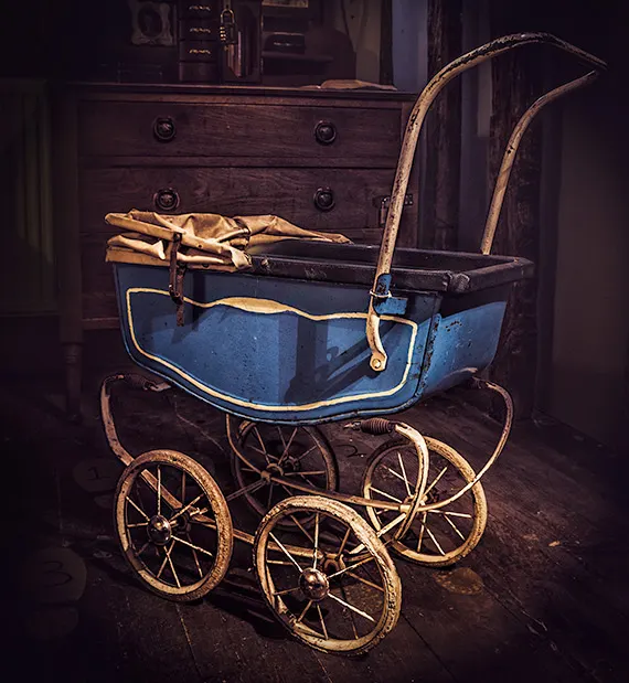 Vintage pram with blue body and wicker wheels displayed indoors beside wooden furniture.