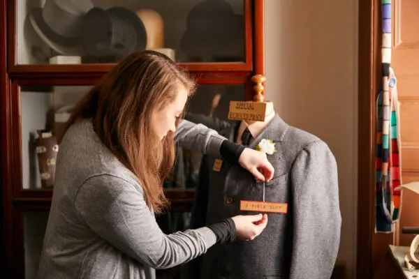 Woman arranging a vintage jacket on a display mannequin in a museum setting.