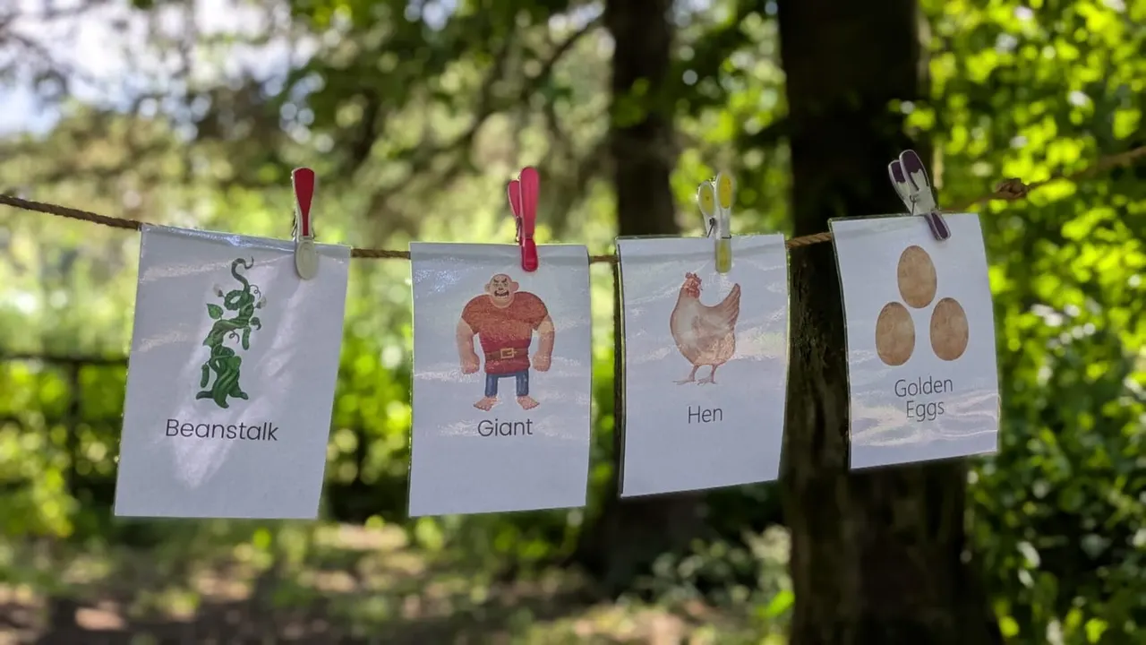 Four illustrated cards pegged to a washing line in a wooded setting, depicting a beanstalk, giant, hen and golden eggs from Jack and the Beanstalk.