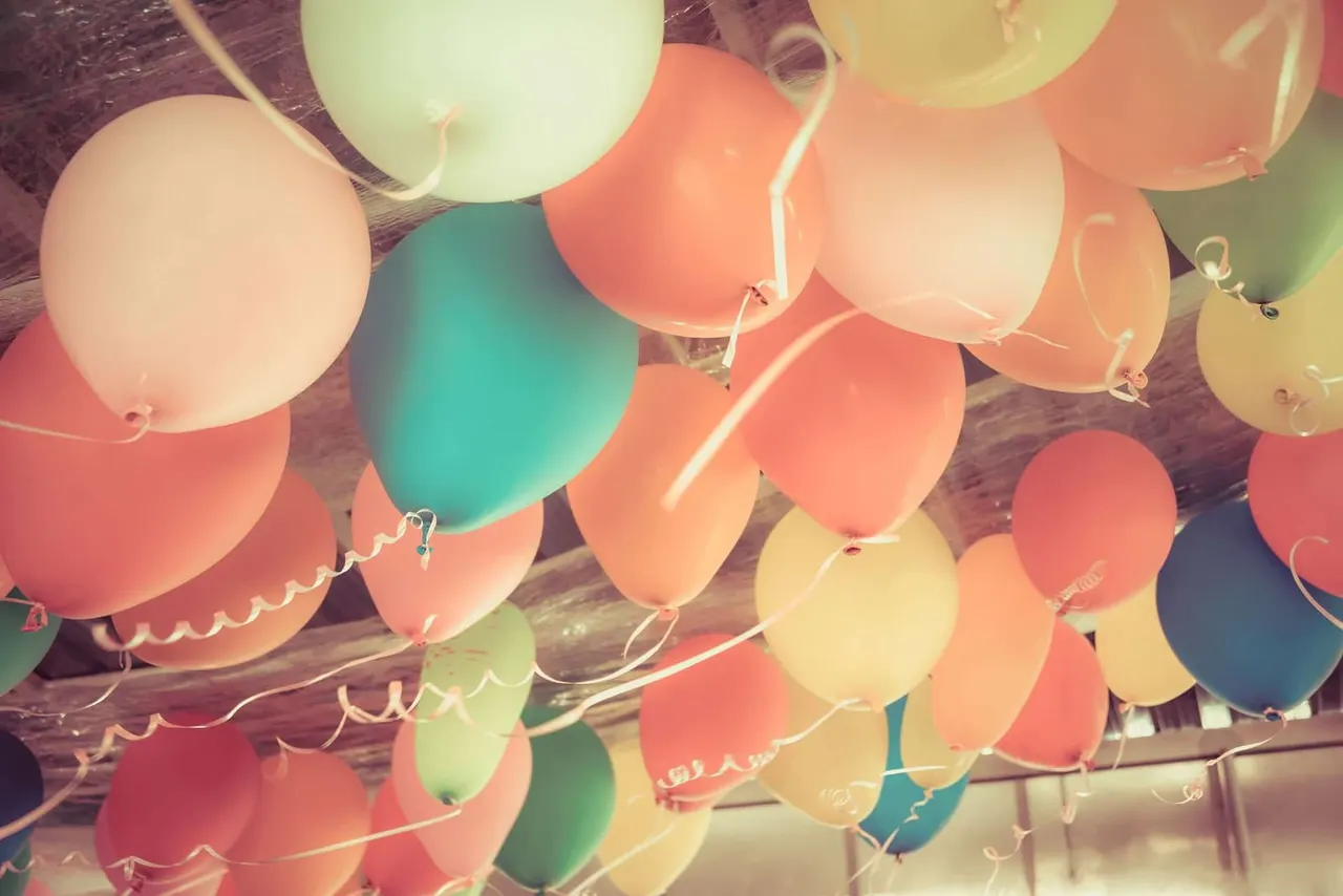 Colourful balloons in red, pink, yellow, green and teal suspended from strings against a wooden ceiling.